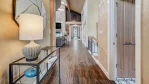 Un hall d’entrée spacieux avec un plancher en bois, une console en verre surmontée d’une lampe, et une porte sur le côté droit.