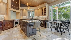 Une cuisine spacieuse dotée d’un grand îlot central, de meubles en bois et d’un coin repas offrant une vue sur l’extérieur.
