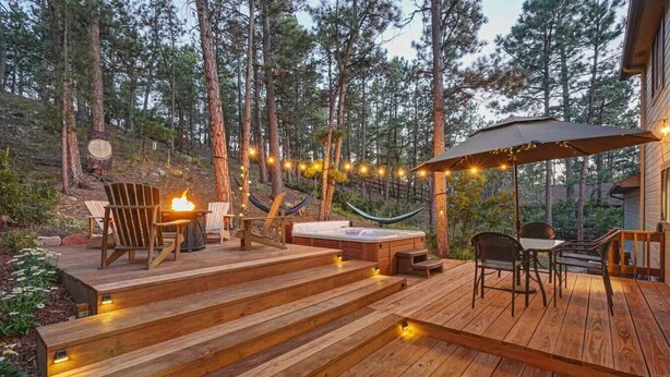 Een houten terras met buitenmeubilair, een jacuzzi en lichtjes.