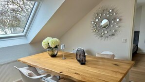 A dining area with a wooden table, white chairs, a vase of flowers, a modern mirror, and a skylight. - Living in Ohligs, attic apartment (Solingen)