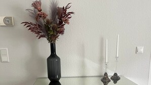 Un bureau à plateau en verre, orné d’un vase de fleurs séchées et de deux bougies.