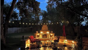 An outdoor patio area with a stone fire pit, seating, and string lights.