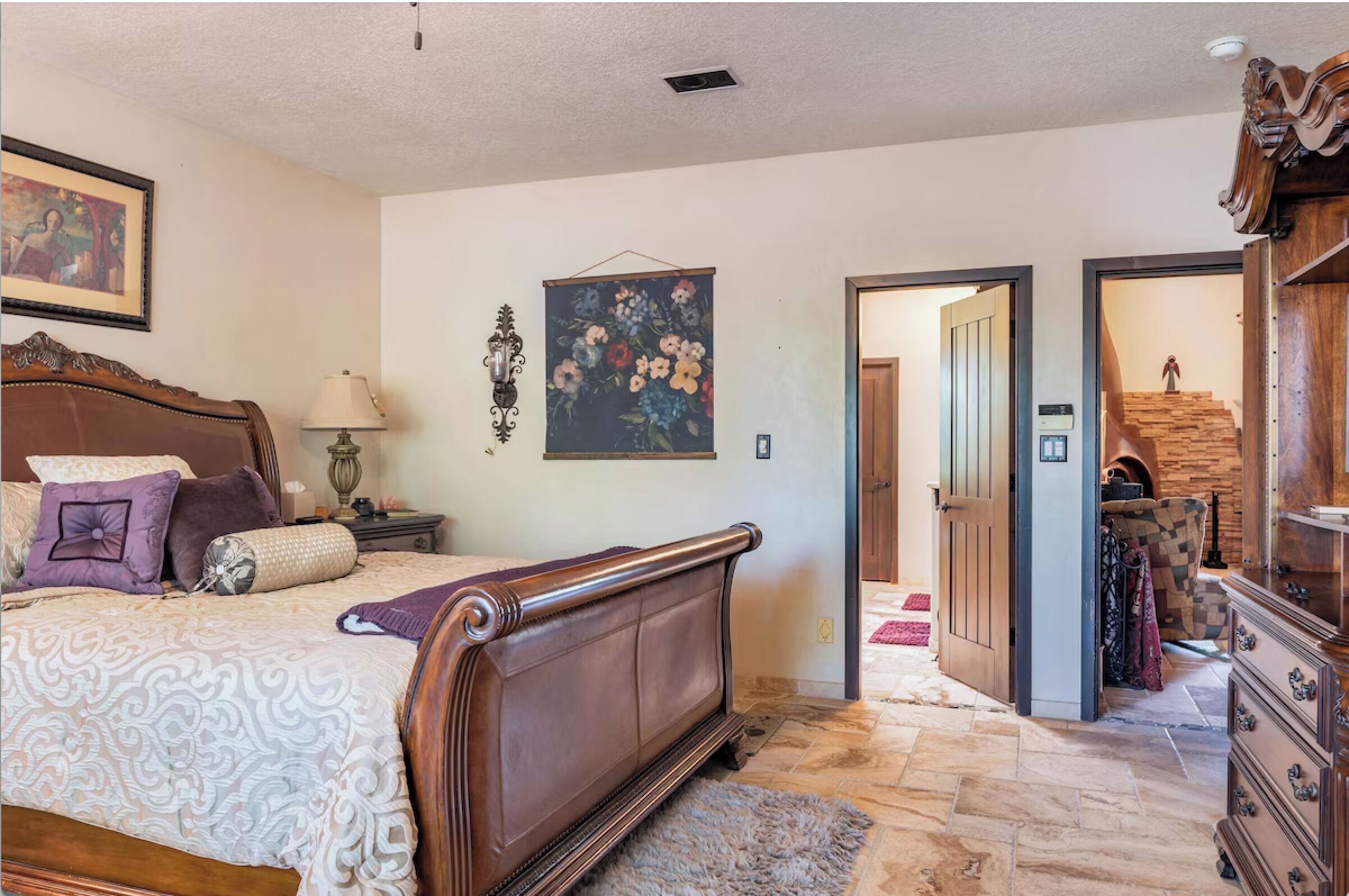 A bedroom with a large bed, a wooden dresser, and a painting on the wall.
