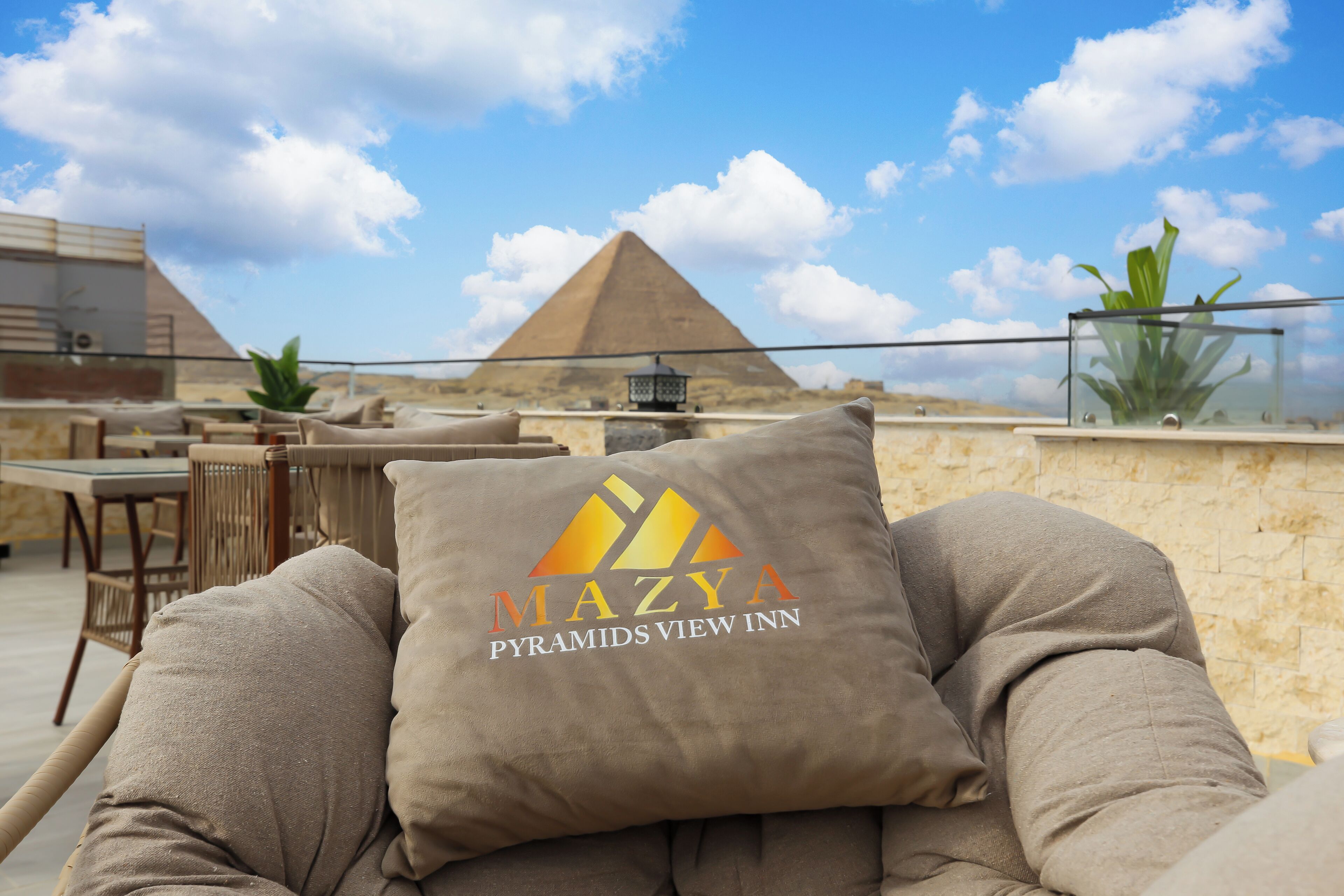 Et loungeområde med udsigt til pyramiderne, med en loungeseng og en pude med hotellets logo.