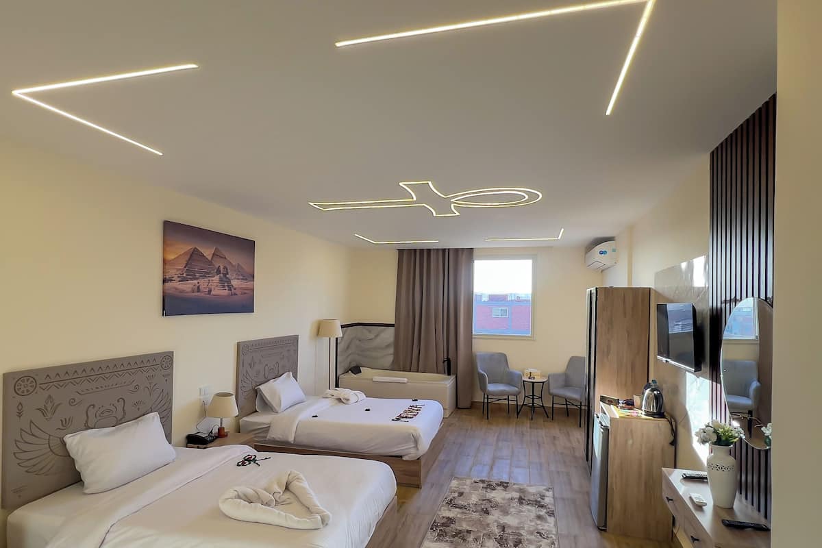 Habitación de hotel con dos camas, televisión, escritorio y ventana con cortinas.