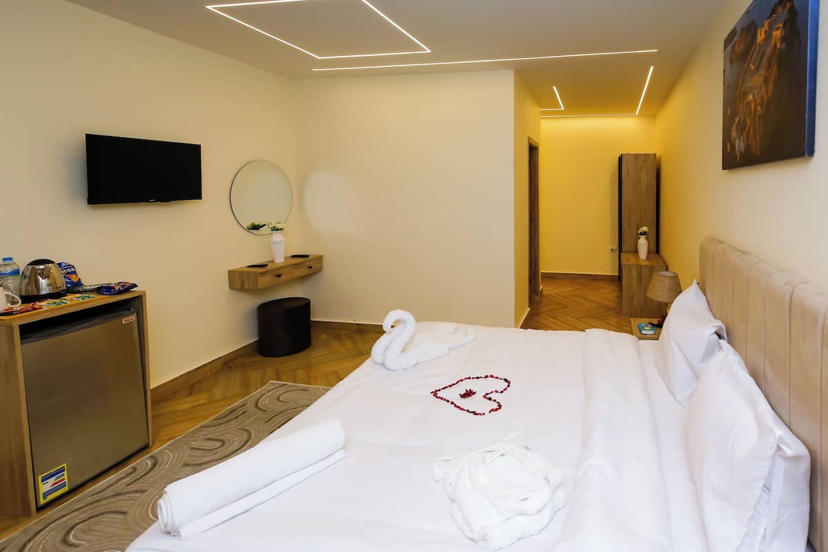 Una habitación de hotel con una cama, televisión, escritorio con computadora, espejo y un pequeño bote de basura.