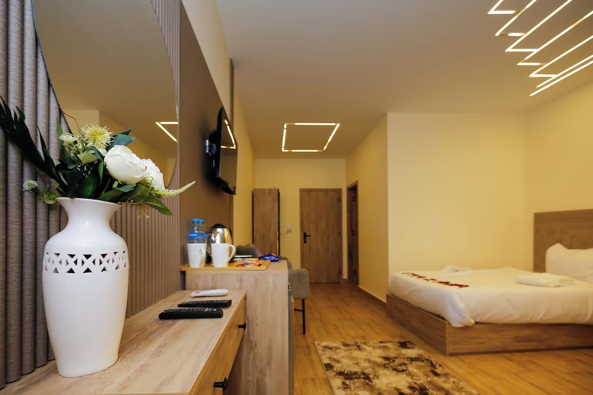 Una habitación de hotel con una cama, un escritorio con un florero, un espejo y un televisor.