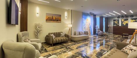 A modern living room with a marble floor, sofas, a flat-screen TV, and wall-mounted lighting.