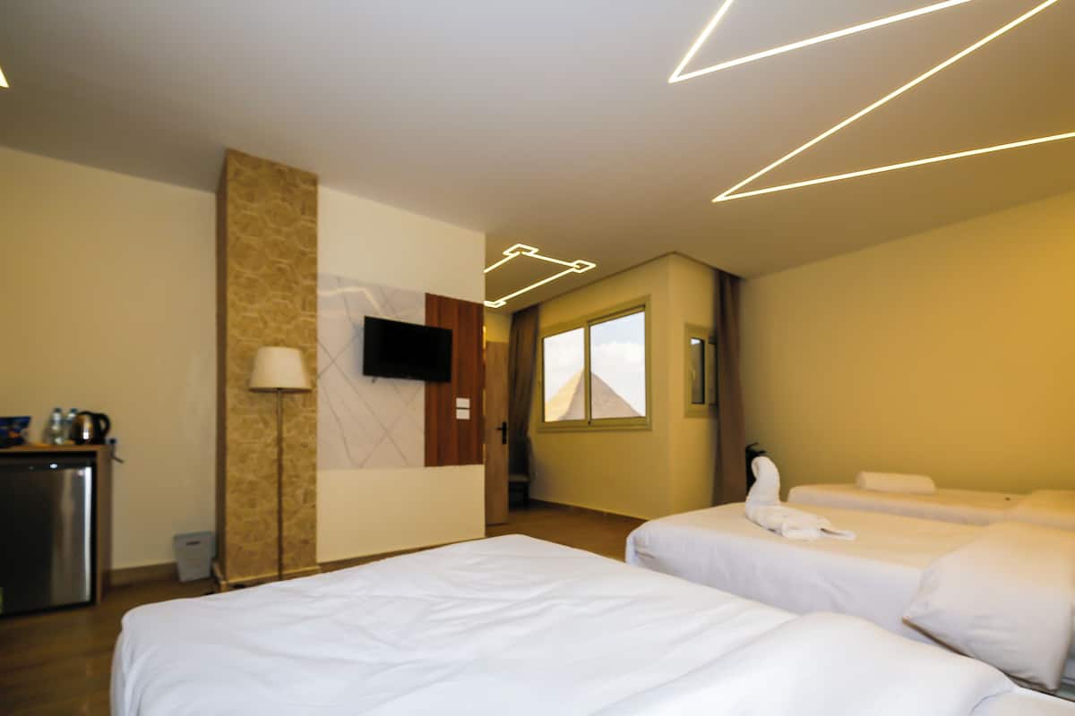 Habitación de hotel con dos camas, un escritorio con hervidor, televisión de pantalla plana y ventana con cortinas.