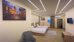 A hotel room with two beds, a desk, a chair, a TV, and a painting of a cityscape. - Mazaya Pyramids View Inn (Giza)