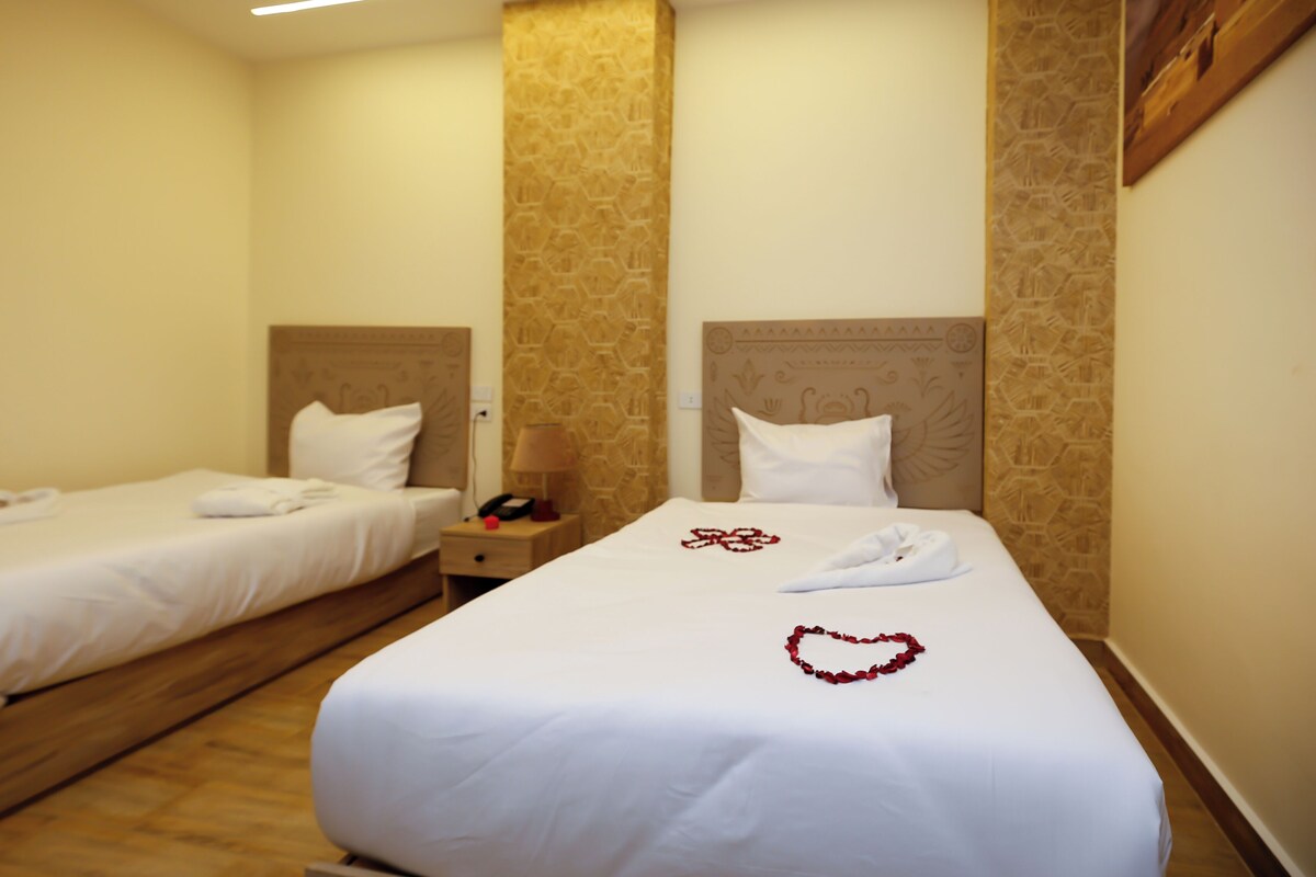 Ein Hotelzimmer mit zwei Einzelbetten, einem Nachttisch mit Lampe und einem an der Wand befestigten Telefon.