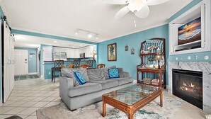 A living room with a grey sofa, a glass coffee table, a fireplace, and a kitchen in the background. - Two Bedroom Updated Condo with Great Amenities (Ocean City)