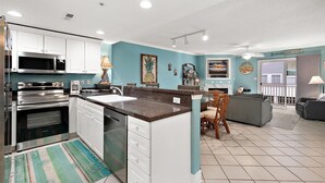 A modern kitchen with white cabinets, a granite countertop, and stainless steel appliances. There is a dining area with a table and chairs, and a living room with a couch and a TV. - Two Bedroom Updated Condo with Great Amenities (Ocean City)