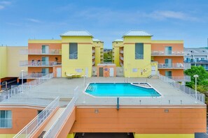 Ein mehrstöckiges Hotel mit einem zentral gelegenen Poolbereich, Balkonen und blauem Himmel.