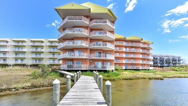 A multi-story hotel with balconies, a wooden dock leading to the water, and a clear sky. - Two Bedroom Updated Condo with Great Amenities (Ocean City)