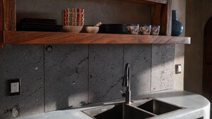 Een keuken met een granieten aanrecht, een roestvrijstalen spoelbak en een houten plank erboven met servies en een vaas.