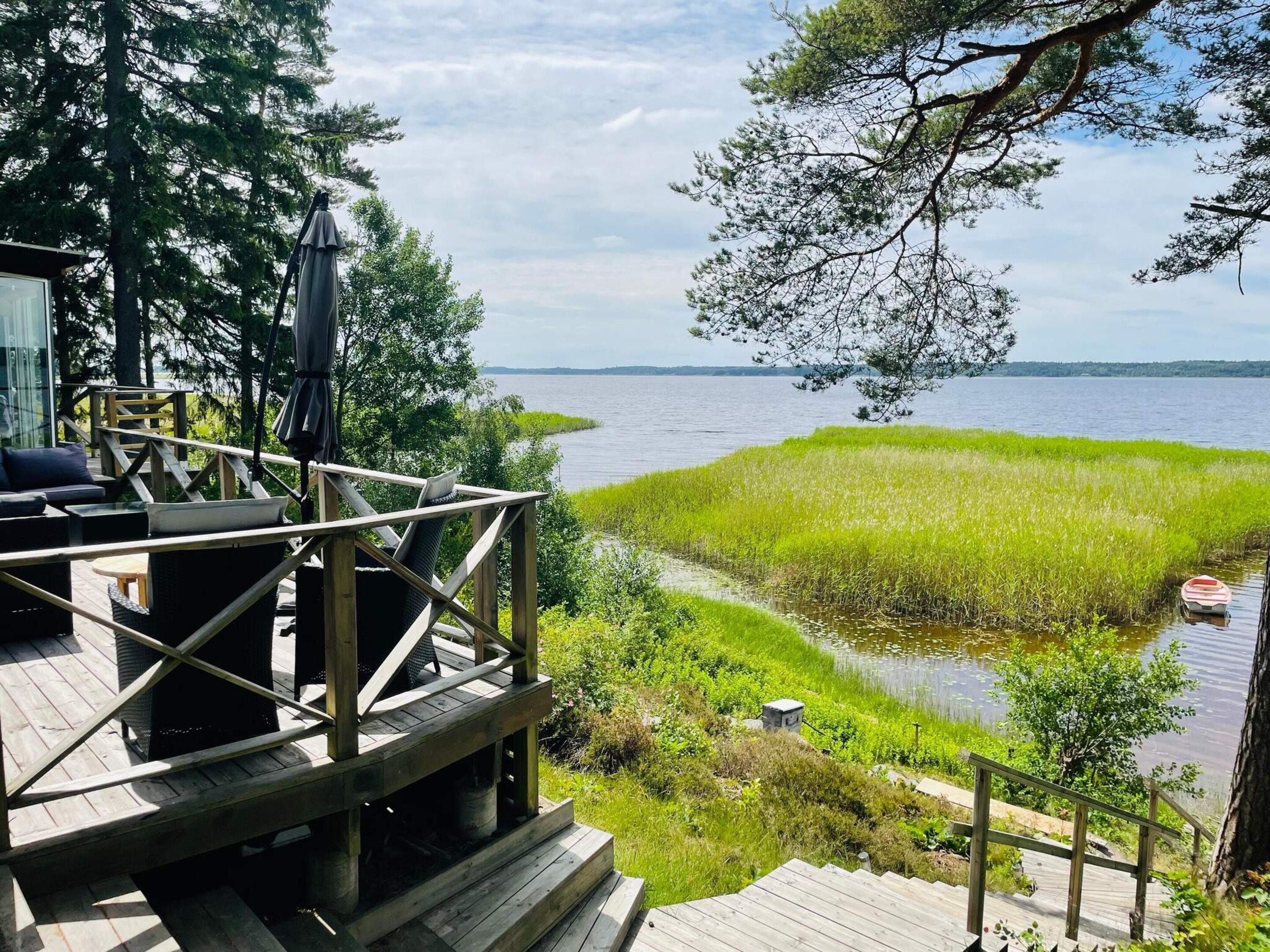 Une terrasse en bois, agréée de mobilier d’extérieur, qui offre une vue sur un lac et une zone herbeuse.