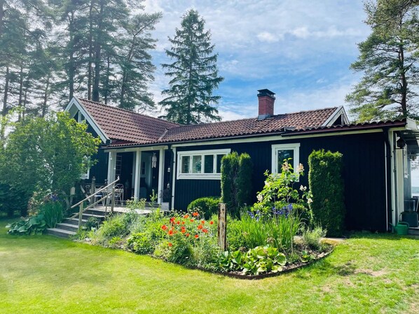 Una casa con techo de tejas rojas, un porche y un jardín con diversas plantas y flores.