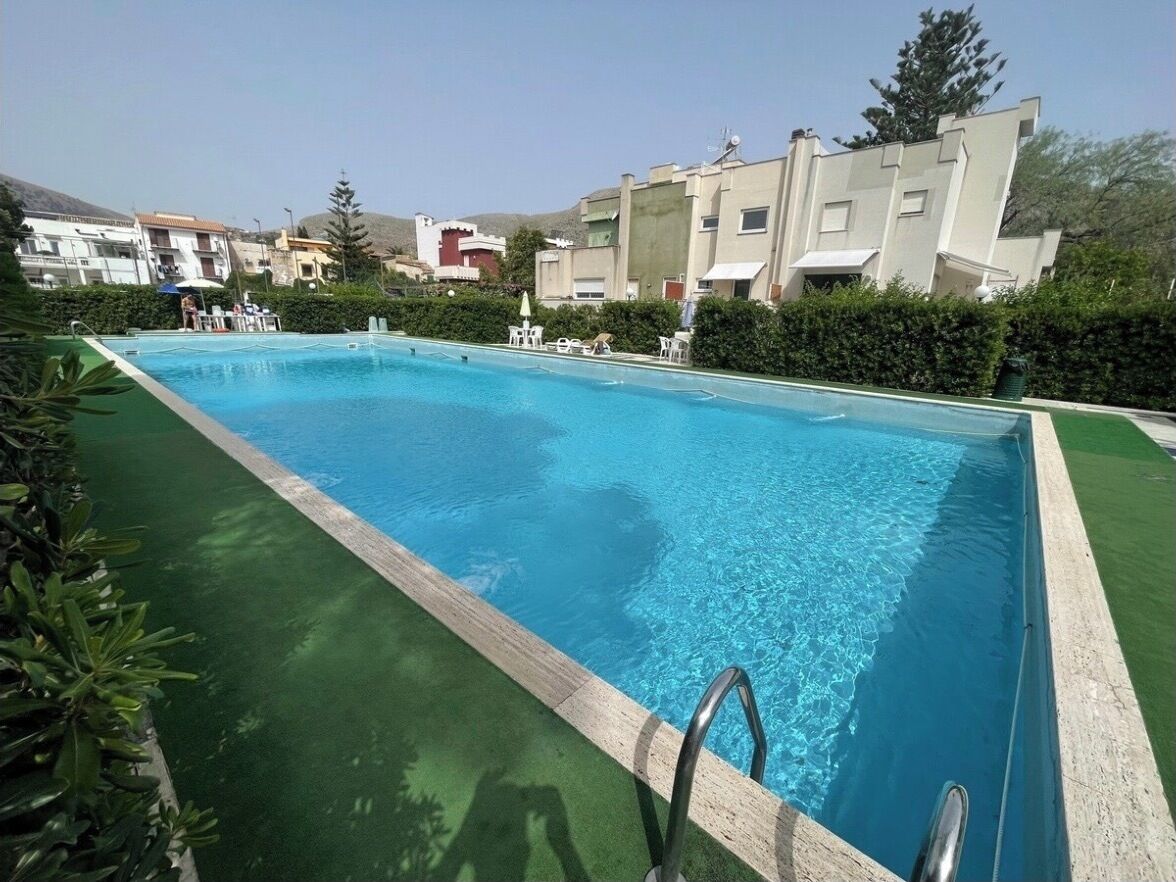 A rectangular swimming pool with clear blue water, surrounded by a green border and a metal ladder.