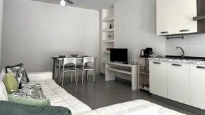 A modern, compact living space with a sofa, dining area, TV, and kitchenette. - Cozy apartment just minutes from the beautiful Mondello beach. (Palermo)