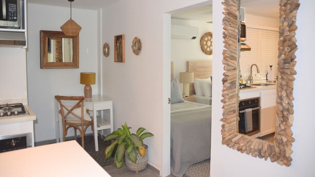 A compact kitchen with a microwave, stove, and sink. A dining area with a table and chair is visible, along with a small potted plant. A mirror with a unique frame is mounted on the wall. - Beautiful Apartment in los Cocos Santa Marta 1 (Santa Marta)
