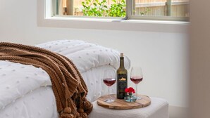 A bedroom with a bed, a bedside table with a bottle of wine and glasses, a window with a view of greenery, and a cozy blanket. - Perfect Basecamp for Outdoor Fun (Driggs)
