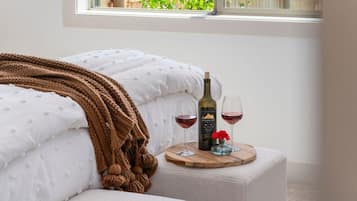 Une chambre avec un lit, une table de chevet sur laquelle se trouve une bouteille de vin et des verres, une fenêtre donnant sur un paysage verdoyant et une couverture douillette.