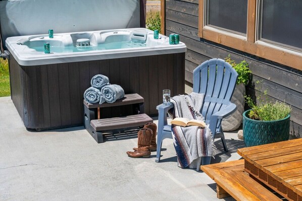 A hot tub with a wooden deck, a chair, a bench, and a table.