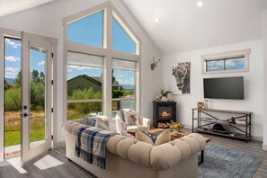 A modern living room with a sofa, fireplace, and large windows.