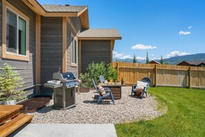 A backyard with a barbecue grill, two Adirondack chairs, and a small fire pit. - Perfect Basecamp for Outdoor Fun (Driggs)