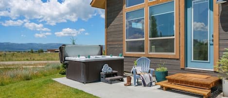 A wooden cabin with a hot tub, outdoor seating, and a view of the mountains.