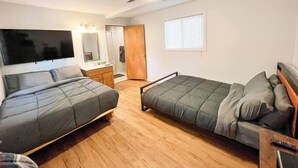 Une chambre avec deux lits, un ventilateur de plafond, une télévision et un plancher en bois.