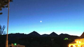Nachtszene mit einem Bergpanorama, einem sichtbaren Mond und einem beleuchteten Gebäude mit einem Schild.