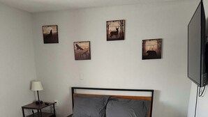 Une chambre à coucher comprenant un lit, une table de chevet, une lampe, un radiateur et quatre tableaux accrochés au mur.