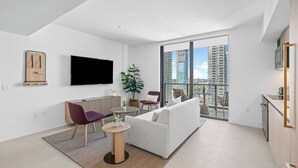 Un soggiorno moderno con divano, poltrone, tavolino, televisore e un balcone con vista sulla città.