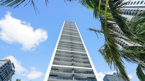 Ein modernes Hochhaus mit mehreren Balkonen, umgeben von Palmen und weiteren Hochhäusern.