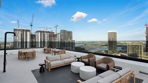 En takterrass med utomhusmöbler, utsikt över stadens silhuett och byggkranar i bakgrunden.
