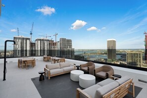 Eine Dachterrasse mit Sitzgelegenheiten im Freien, Blick auf die Skyline der Stadt und Baukräne im Hintergrund.