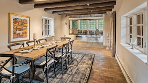 A dining area with a wooden table and chairs, a rug, and a painting on the wall.