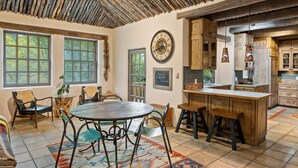 A rustic interior with a round dining table, wooden cabinets, and a large window offering a view of trees.
