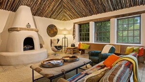 A cozy living room with a fireplace, comfortable seating, and large windows offering a view of the outdoors.