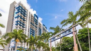 Un hotel moderno con numerosi balconi, palme e un cielo azzurro intenso.