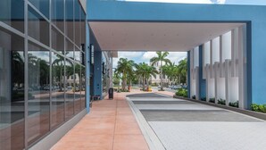 Un edificio moderno con ampie vetrate, una tettoia e palme sullo sfondo.