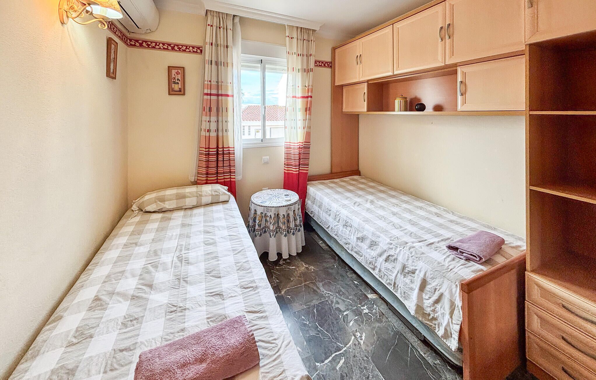 A small, compact room with two single beds, a round table, and a wooden cabinet.