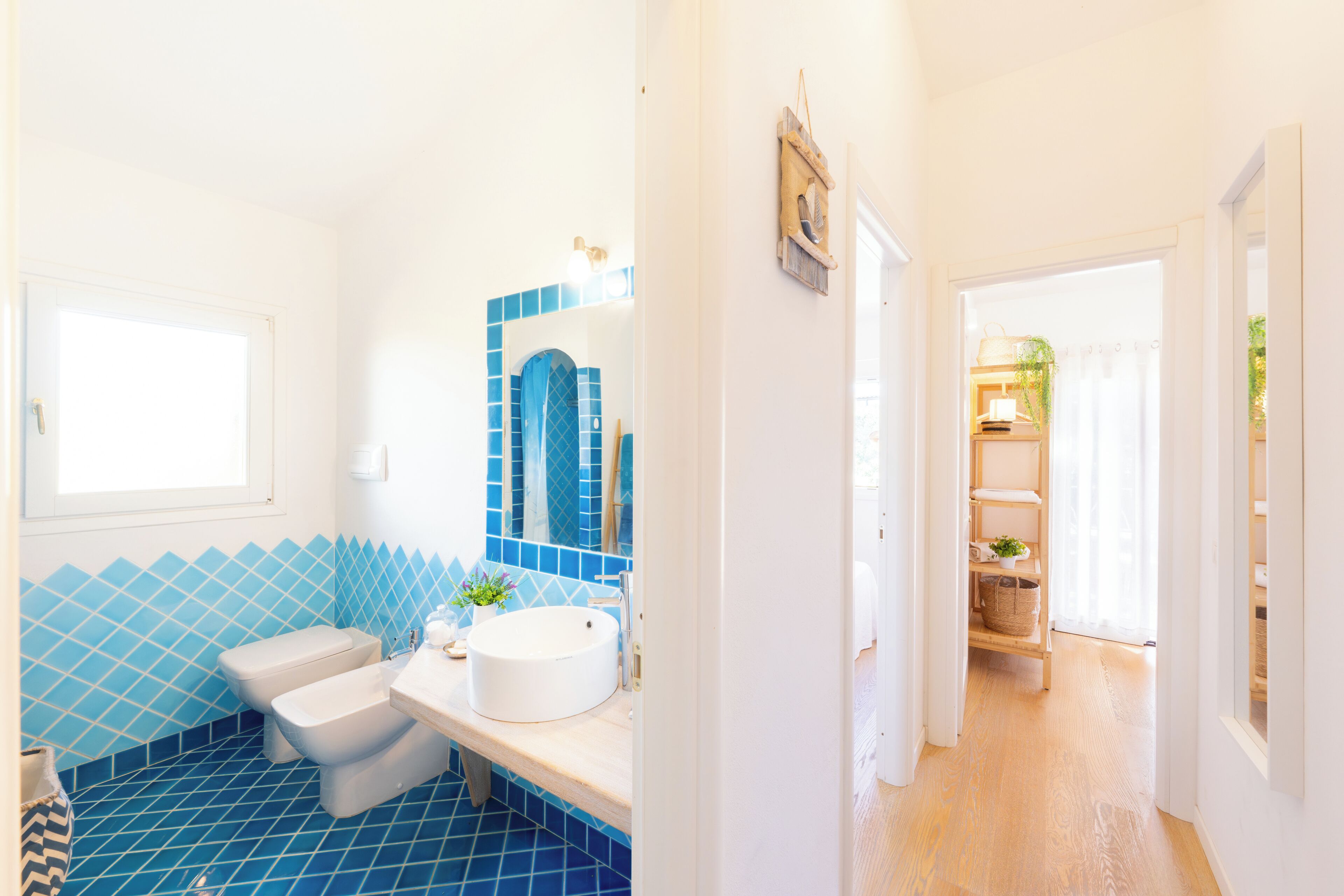 Een badkamer met een blauwe betegelde vloer, een witte wastafel en een spiegel met blauwe lijst.