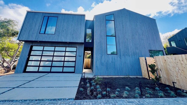 Ett modernt hus i två våningar med garage, stora fönster och en välskött trädgård.
