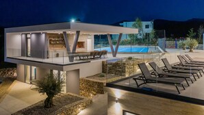 Una casa moderna con un bar en la azotea, una piscina y sillones de descanso.