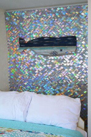 A bed with a white pillow and a blue patterned bedspread, against a wall with a reflective, scale-like pattern. - Bay Watch Resort Oceanfront Condo (North Myrtle Beach)