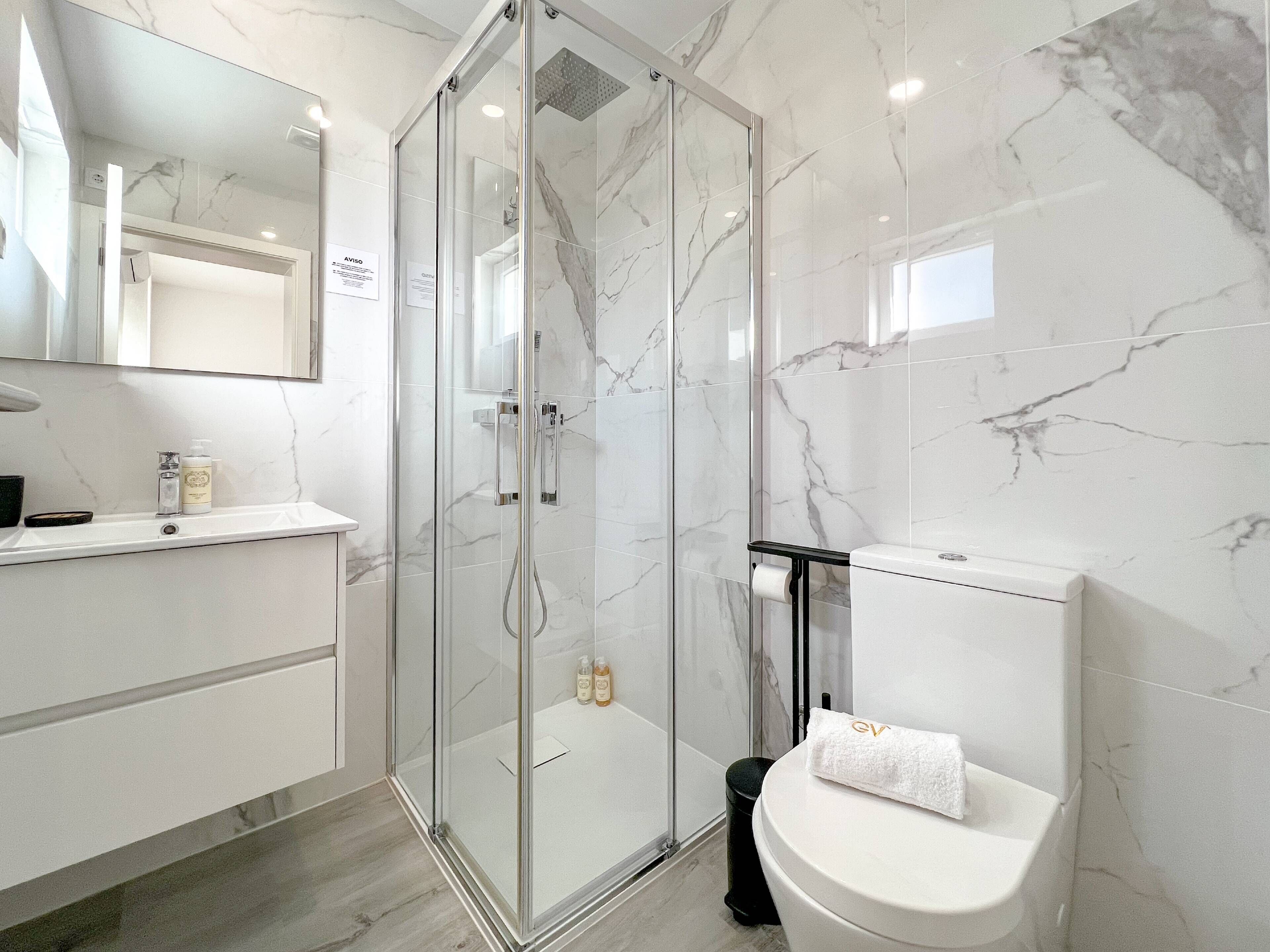 A modern bathroom with a glass-enclosed shower, a white toilet, and a marble-tiled wall.