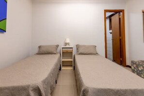A small, clean room with two single beds, a nightstand with a lamp, and a door leading to another room. - Casa ampla com piscina e churrasqueira  (Carapicuíba)